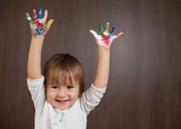 un enfant souriant lève les mains pleines de peinture